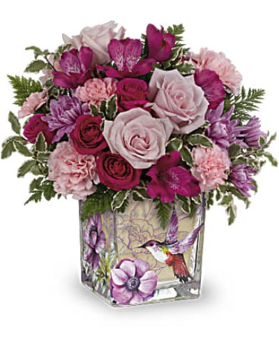 Delicate and enchanting, this bouquet evokes the charm of a hummingbird dancing through a hidden garden. Presented in a vintage-style glass cube, it’s a magical gift for Mother’s Day or any moment worth celebrating.

Featuring hot pink spray roses, rich pink alstroemeria, lavender cushion chrysanthemums, soft pink carnations, miniature pink blooms, and lush greenery including leatherleaf fern and pitta negra.